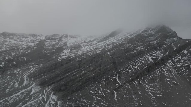 snow season rocky mountain footage. flying up hight to the mountain in winter snowy day. black color huge rock with snow on top. myst covered the peak