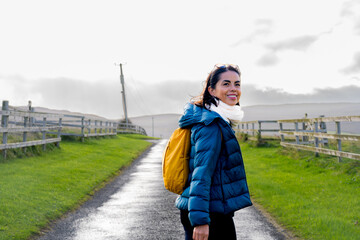 Smiling and exploring latin woman with a yellow backpack and gray jacket smiles enjoying a...