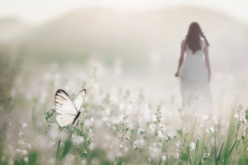 a white butterfly flies free in the middle of a flowery meadow while a woman walks in the background, abstract concept - 696027802