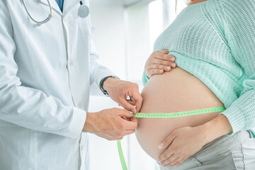 Side view of a pregnant woman middle body section exposing her belly while doctor uses a measuring...