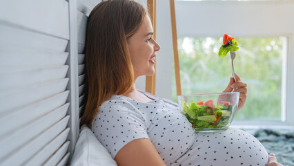 Side view shot of happy pregnant woman eating fresh salad at home