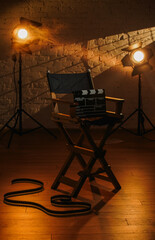 Close up shot of cinema clapperboard standing on director's chair, projectors at the background, warm light, film reel on the floor.