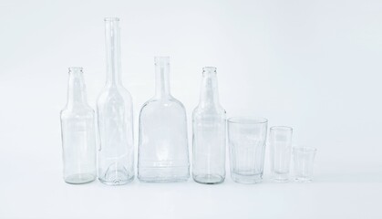 On a light background on the table in the foreground there are empty glass bottles of different sizes, glasses and glasses.  Glassware with zero waste concept, zero waste production, clean environment