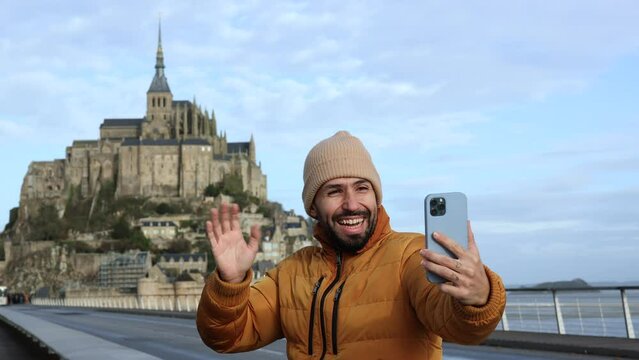 adult man on vacation has a video call with his family and friends with his phone at Mont Saint-Michel in France
