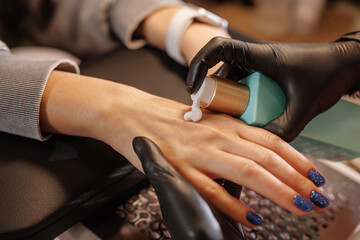 manicurist applies cream to client's hands for hand care in beauty salon