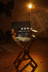 Close up shot cinema clapperboard standing on director's chair popcorn scattered on surface, spotlight with warm light standing at the back.