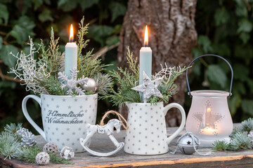 Weihnachts-Arrangement mit Kerzen und Koniferenzweigen in Milchkanne und Tasse im Wintergarten
