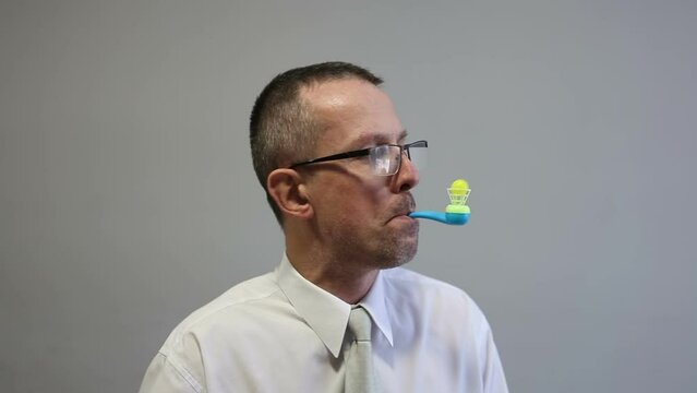 A man is playing in the office, blowing into a tube with a ball. Floating ball game. Free time at work.
