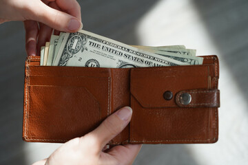 Woman taking out US dollars (banknotes) from an old (deteriorating) brown wallet