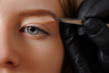 The master makes the client eyebrow correction with tweezers.