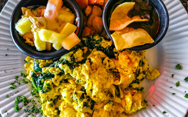 Breakfast scrambled eggs spinach fruit potatoes nicely arranged on plate.