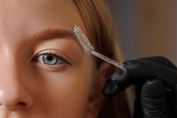 Master eyebrowist makes eyebrow correction to a girl in a beauty salon, close-up