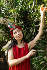 Lovely brunette in red dress, turban decorated with of colorful feathers stands in nature. 
