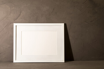 White frame leaning on dark plaster wall
