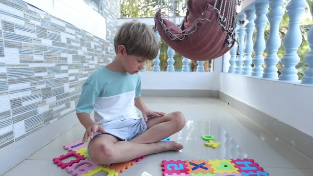 A cute boy is sitting on the balcony in front of an alphabet puzzle mat and is looking forward to entering.