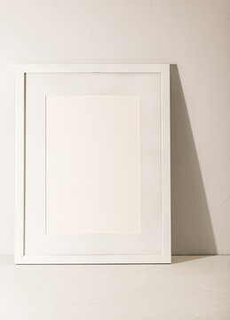 White frame leaning on white plaster wall
