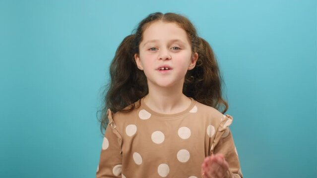 Portrait of pretty positive preteen girl child smiling and talking to camera, happy cheerful expression, posing isolated over plain blue color background wall in studio. Childhood concept