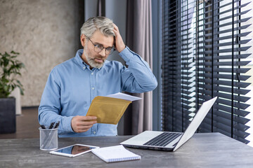 Sad unhappy man sitting at workplace inside office, senior mature gray-haired businessman taking...