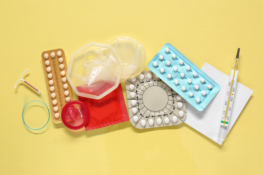 Contraceptive pills, condoms, intrauterine device and thermometer on yellow background, flat lay. Different birth control methods