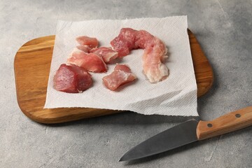 Paper towel, pieces of meat and knife on grey table