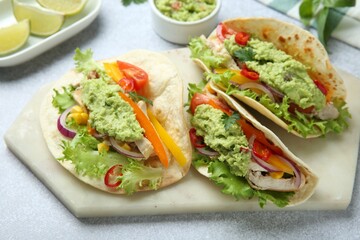 Delicious tacos with guacamole, meat and vegetables on light grey table, closeup