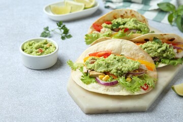 Delicious tacos with guacamole, meat and vegetables on light grey table