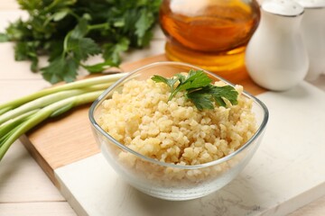 Delicious bulgur with parsley in bowl and products on table, closeup