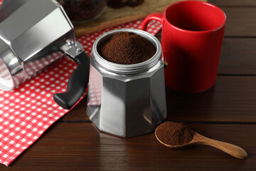 Moka pot with ground coffee, spoon and red cup on wooden table