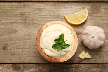 Tasty sauce with garlic, parsley and lemon on wooden table, flat lay. Space for text