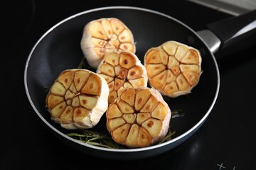 Frying pan with fried garlic and rosemary on stove, closeup
