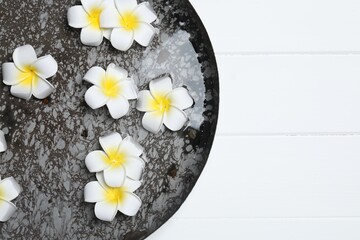 Bowl of water with plumeria flowers on white wooden table, top view and space for text. Spa treatment