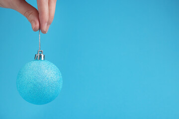Woman holding glitter Christmas ball on light blue background, closeup. Space for text