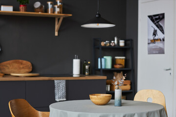 Part of studio kitchen interior in minimal style with use of natural materials, focus on round clothed table with bowl and vase on top and wooden chairs