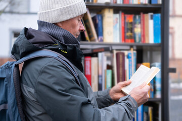 mature man, senior 60 years old stands by street urban library shelf, reading book, reading and...