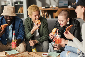 Medium long shot of multi-ethnic group of cheerful young people eating pizza and drinking fizzy drinks at home