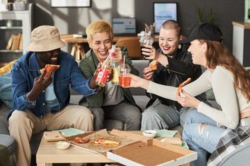 Medium full shot of diverse group of laughing students toasting with soda while holding slices of...