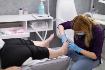 A beautician removes cuticles around her client's toenails.