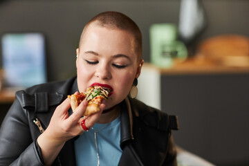 Medium close up shot of stylish young girl with buzz cut eating slice of delicious pizza