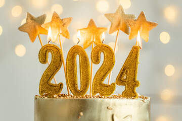 Big golden New Year cake decorated with golden stars and candles against bokeh lights background....