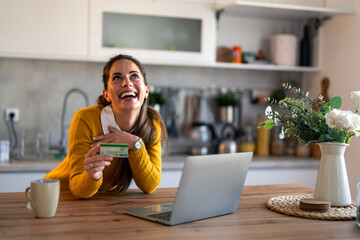 Enthusiastic charming millennial woman feeling excited using laptop holding credit card satisfied...