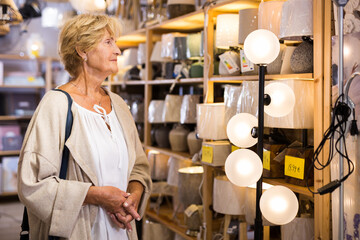Senior woman looking for new lamp at store of household goods