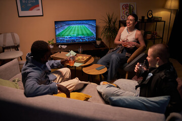 High angle shot of three diverse young students relaxing in living room talking and enjoying soft...
