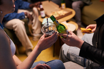 Side view close up of female hands toasting with soft drinks enjoying home party with friends at...