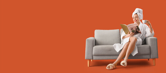 Young woman after shower with cup of coffee reading magazine on grey sofa against orange background...
