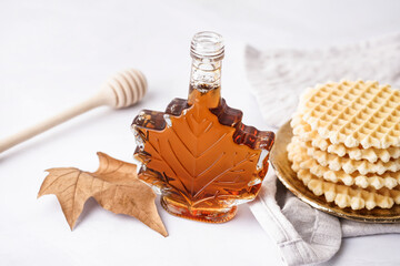 Bottle of tasty maple syrup and waffles on grey background
