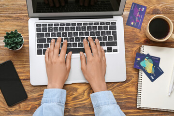 Woman with laptop and credit cards shopping online on wooden background - obrazy, fototapety, plakaty