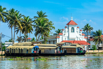 Old colonial Saint Thomas catholic church on the coast of Pamba river, with palms and anchored...