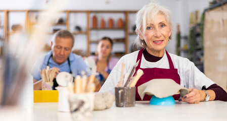 Elderly woman learns to carve figured dishes from clay