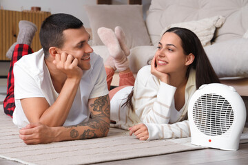 Young couple warming near electric fan heater at home