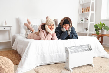 Young couple with puffers warming near radiator in bedroom